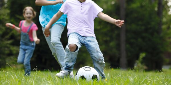 Kinder spielen mit Fussball auf einer Wiese
